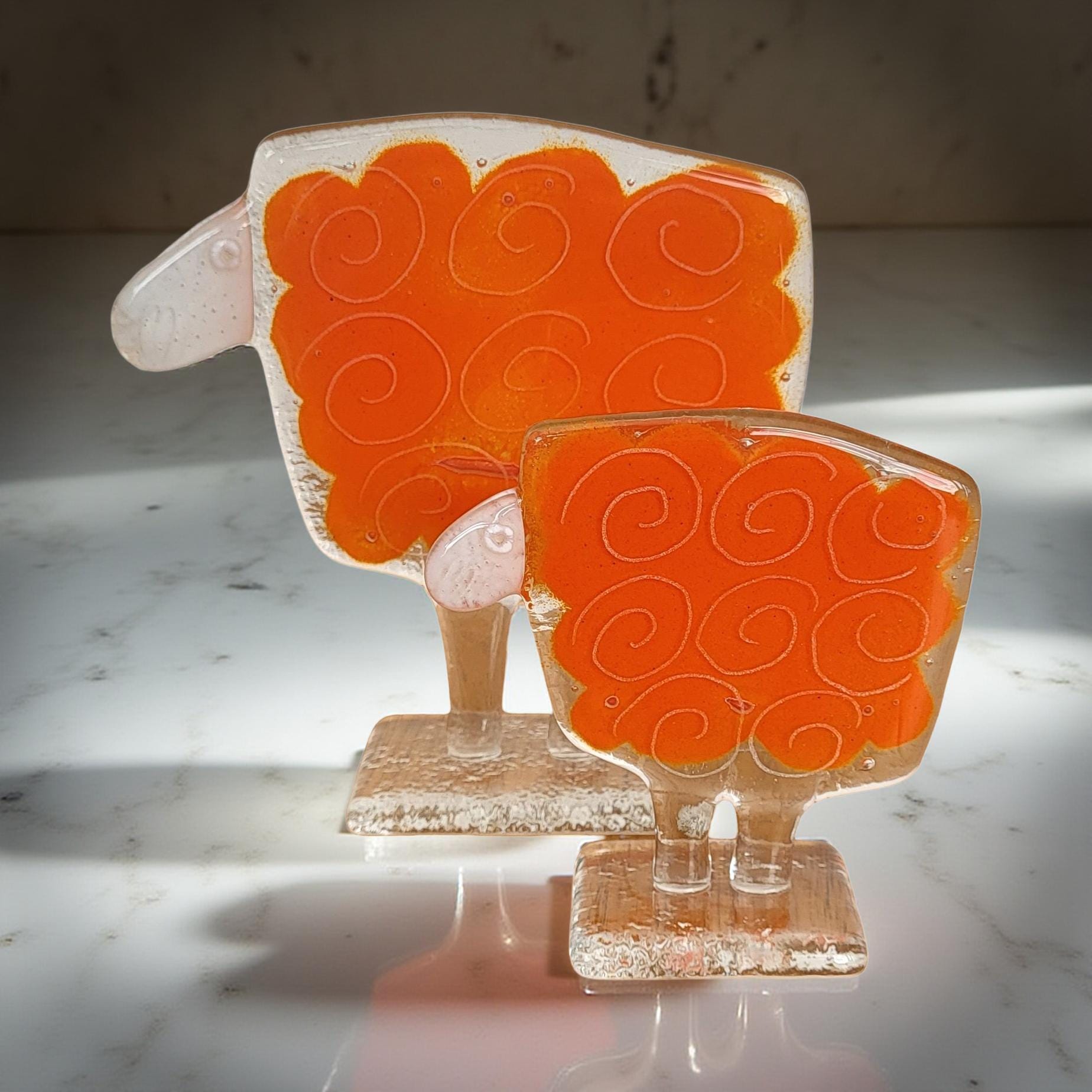 two glass sculptures of sheep, one larger and one smaller, both with orange and white swirl designs on their bodies.