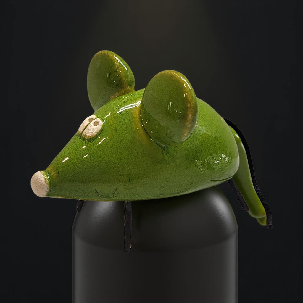 A green ceramic mouse figurine is sitting on top of a black container against a dark background.