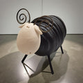 A black metal sculpture of a sheep with curved horns is displayed on a concrete floor.