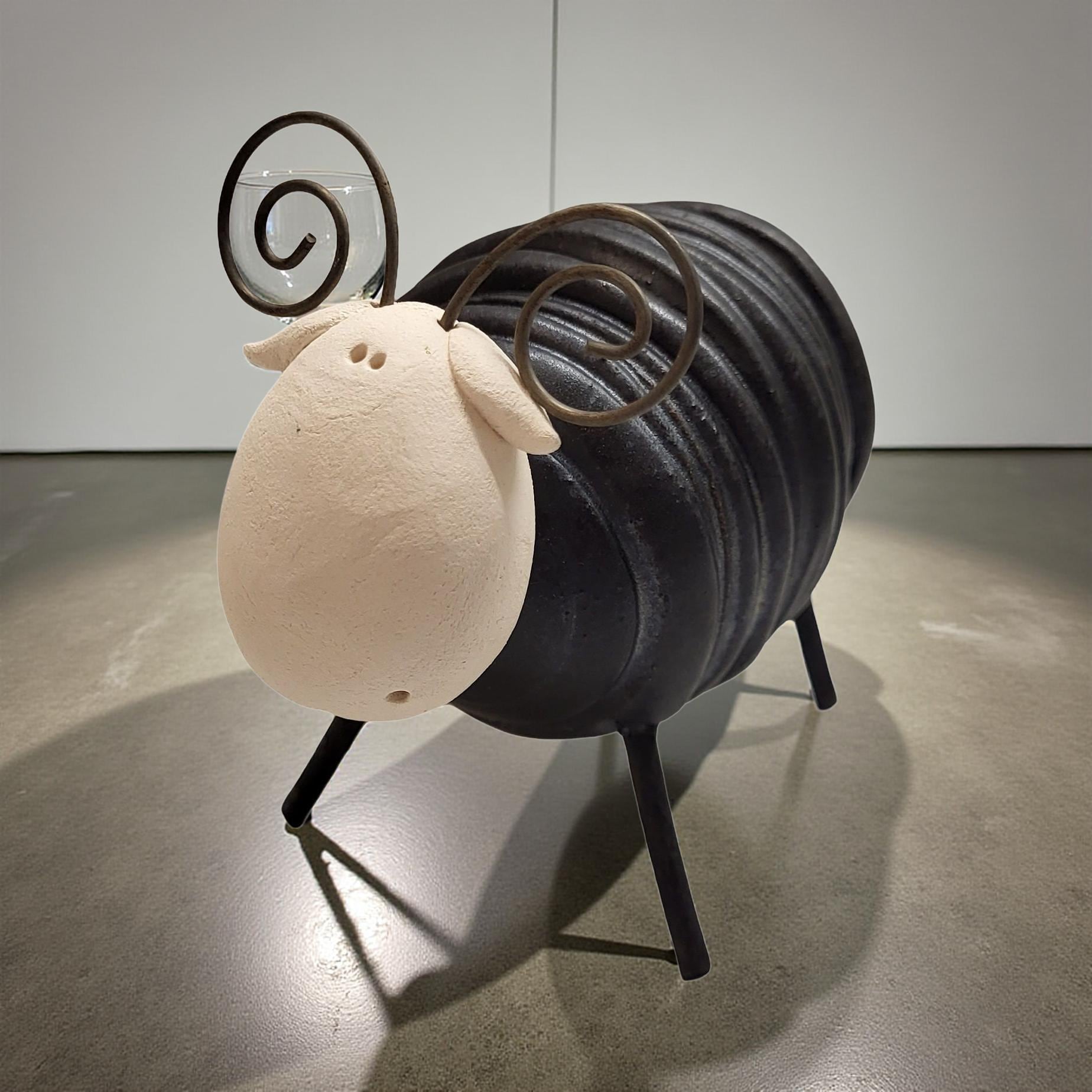 A black metal sculpture of a sheep with curved horns is displayed on a concrete floor.