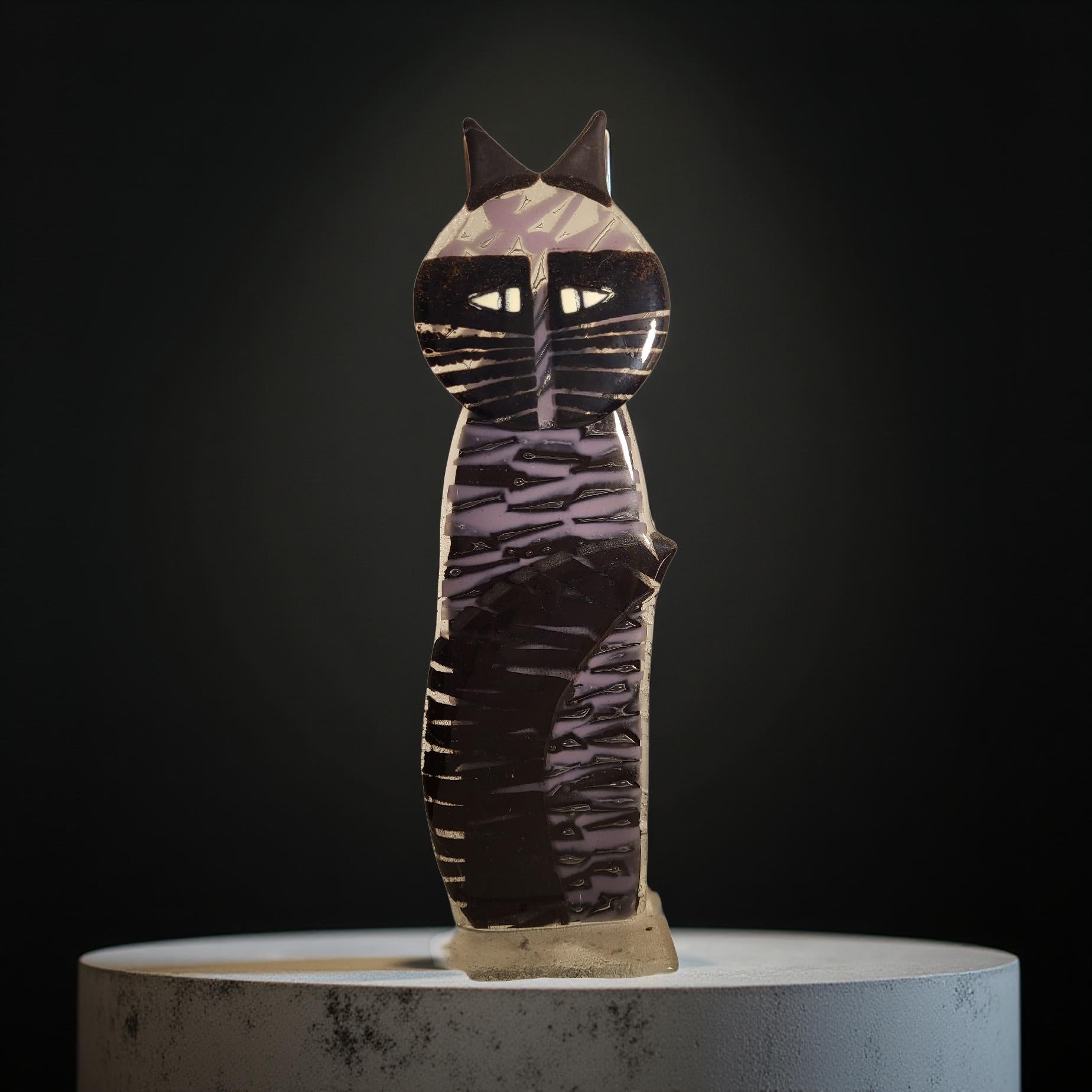 A ceramic cat figurine with a striped pattern and pointed ears is displayed on a white pedestal against a dark background.