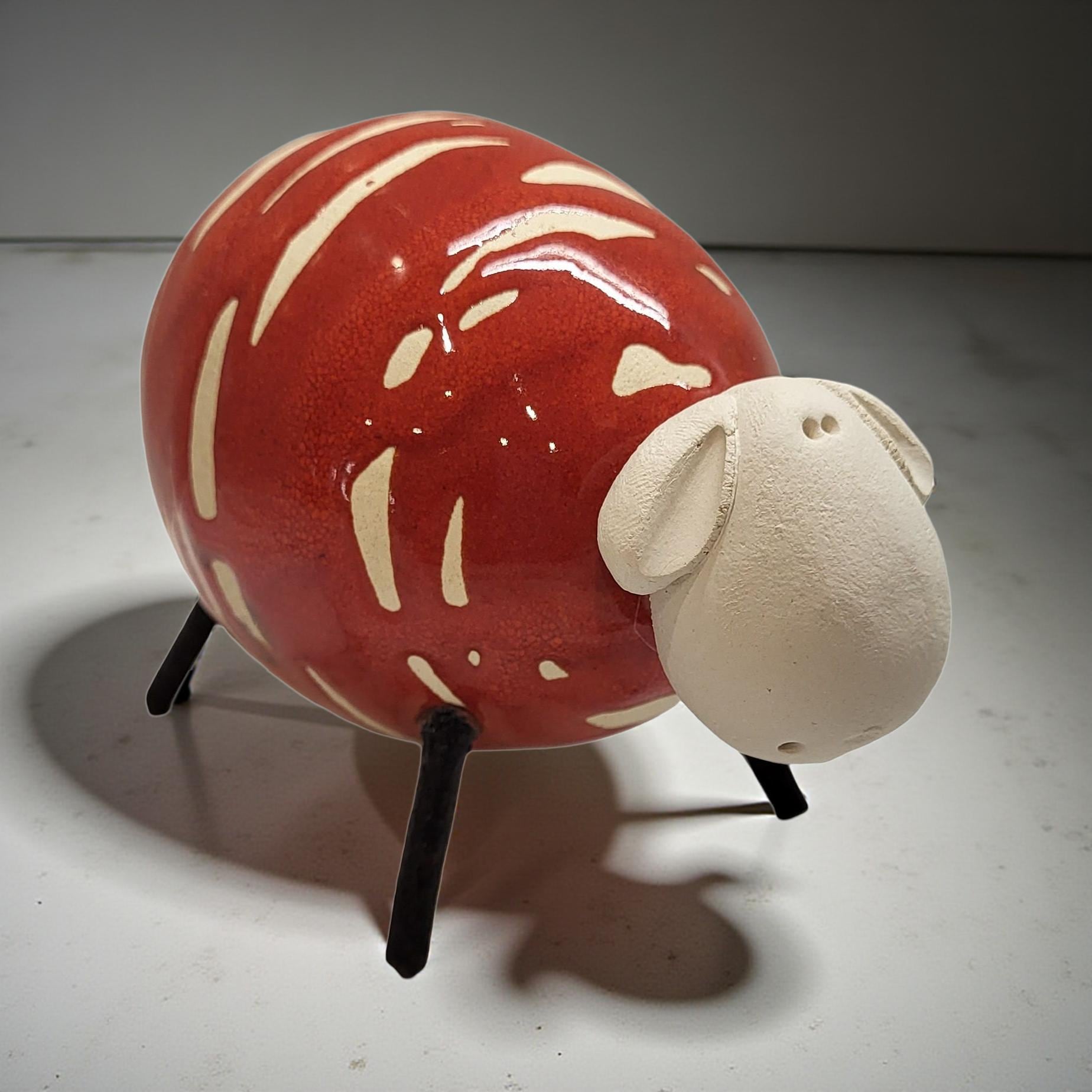 A red and white ceramic sheep figurine is sitting on a white surface.