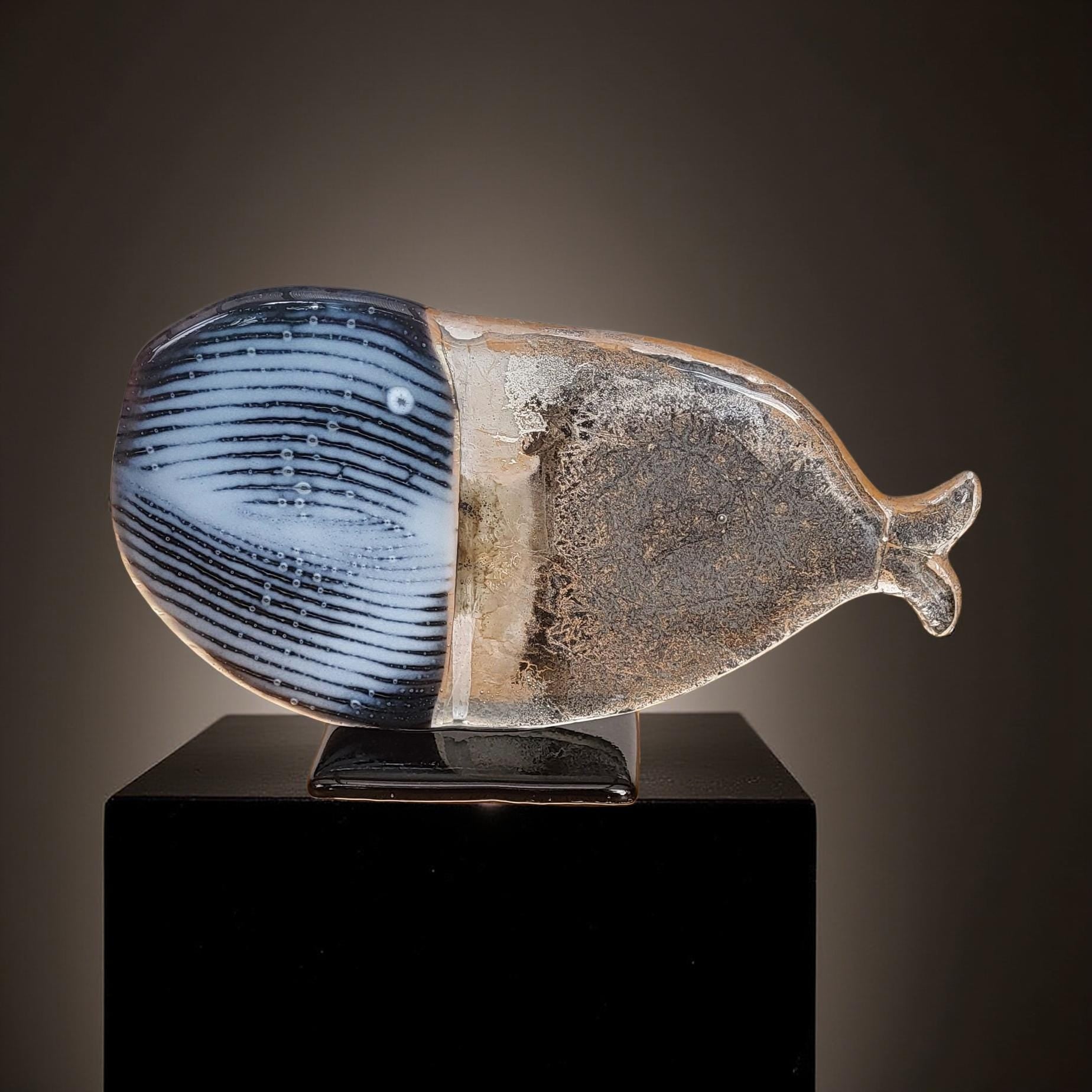 a glass sculpture of a whale, which is displayed on a black pedestal.