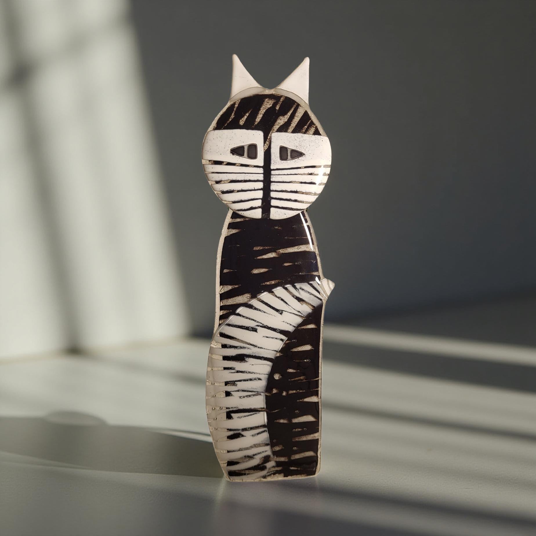 A black and white cat figurine with a unique, abstract design stands on a white surface, casting a shadow.