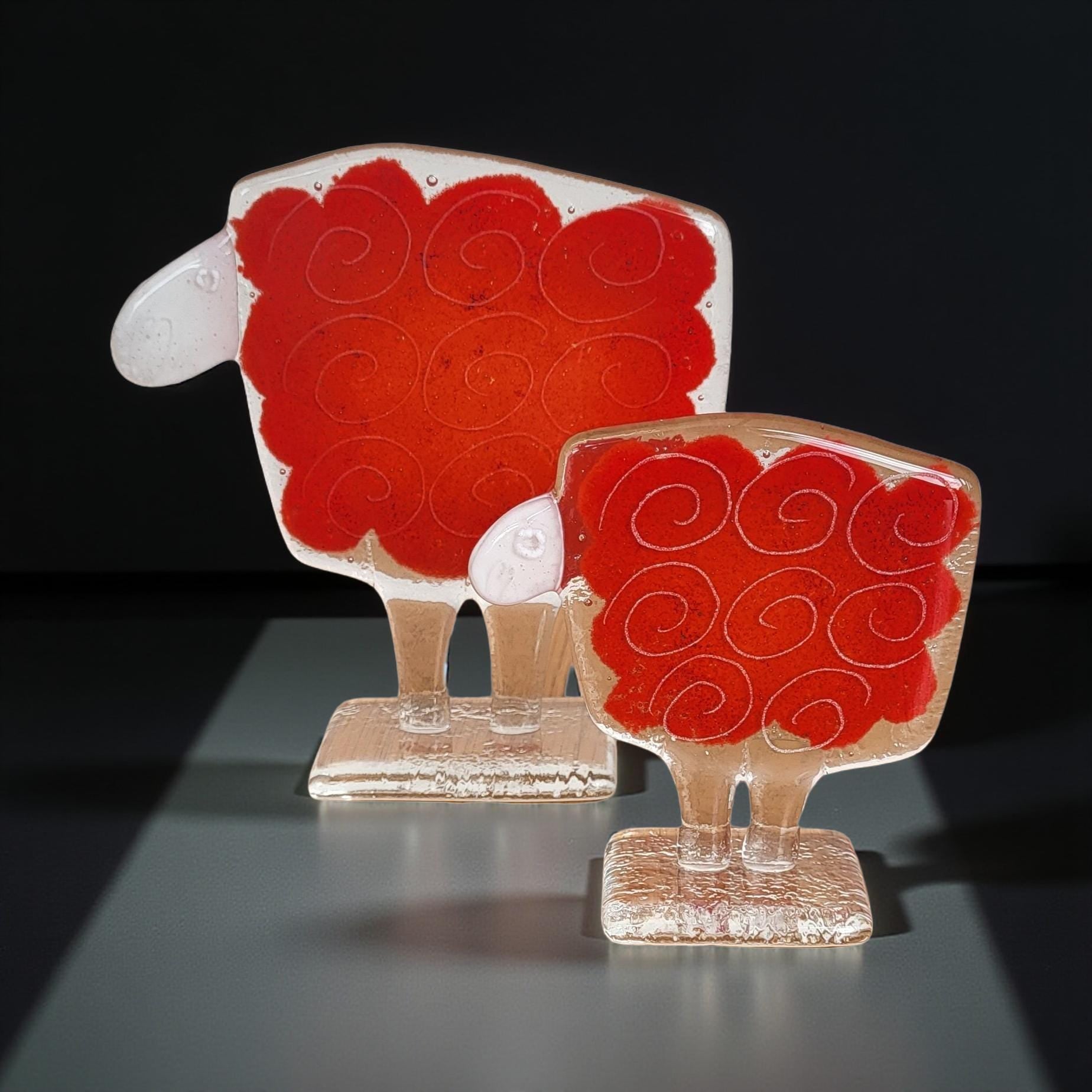 Two glass sculptures of sheep, one larger and one smaller, both with red and white designs.