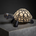 A ceramic turtle figurine with a black and beige color scheme, sitting on a gray surface.