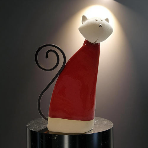 A ceramic cat figurine wearing a red sweater and standing on a black pedestal.