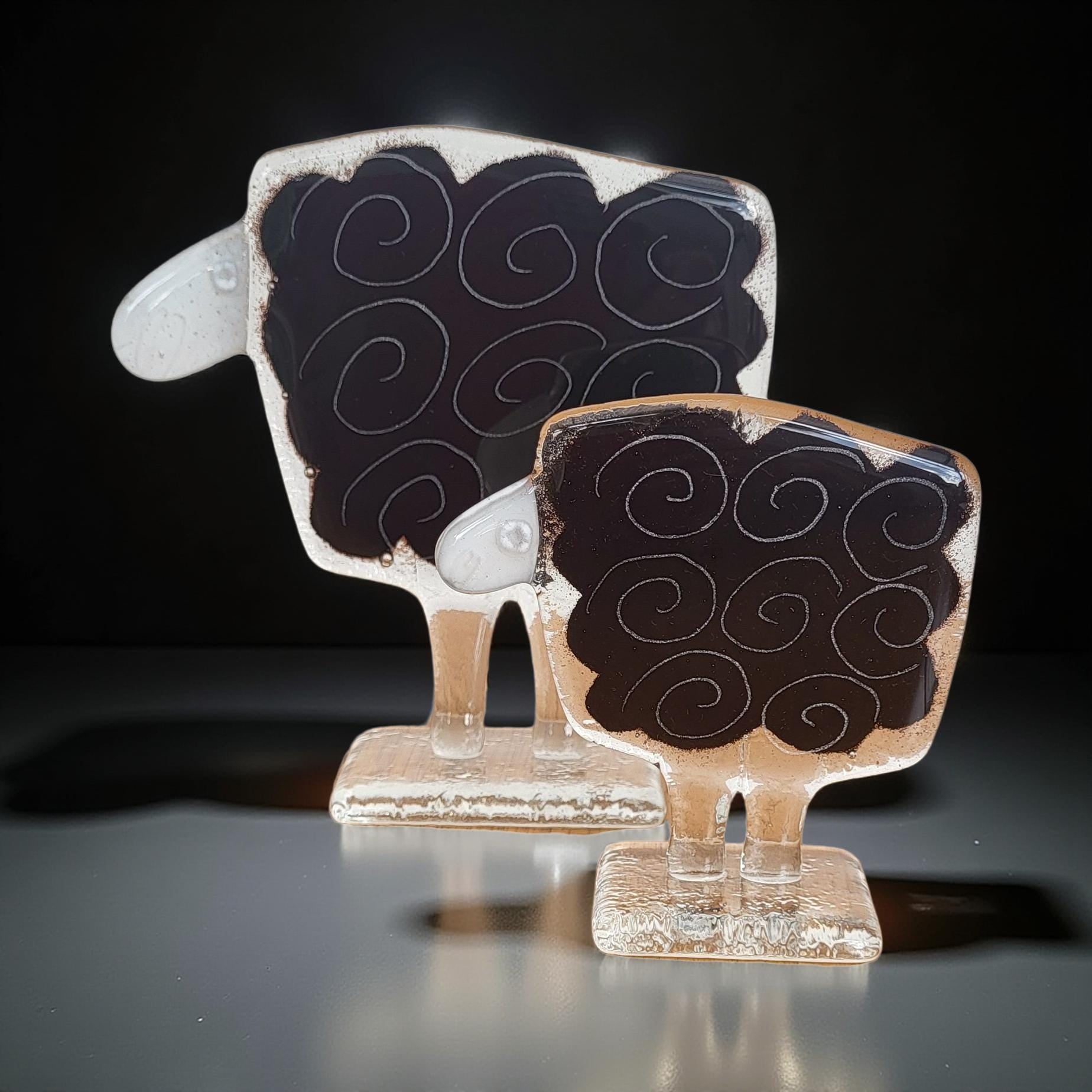 Two glass sculptures of sheep, one larger and one smaller, both with black and white swirl designs on their bodies.