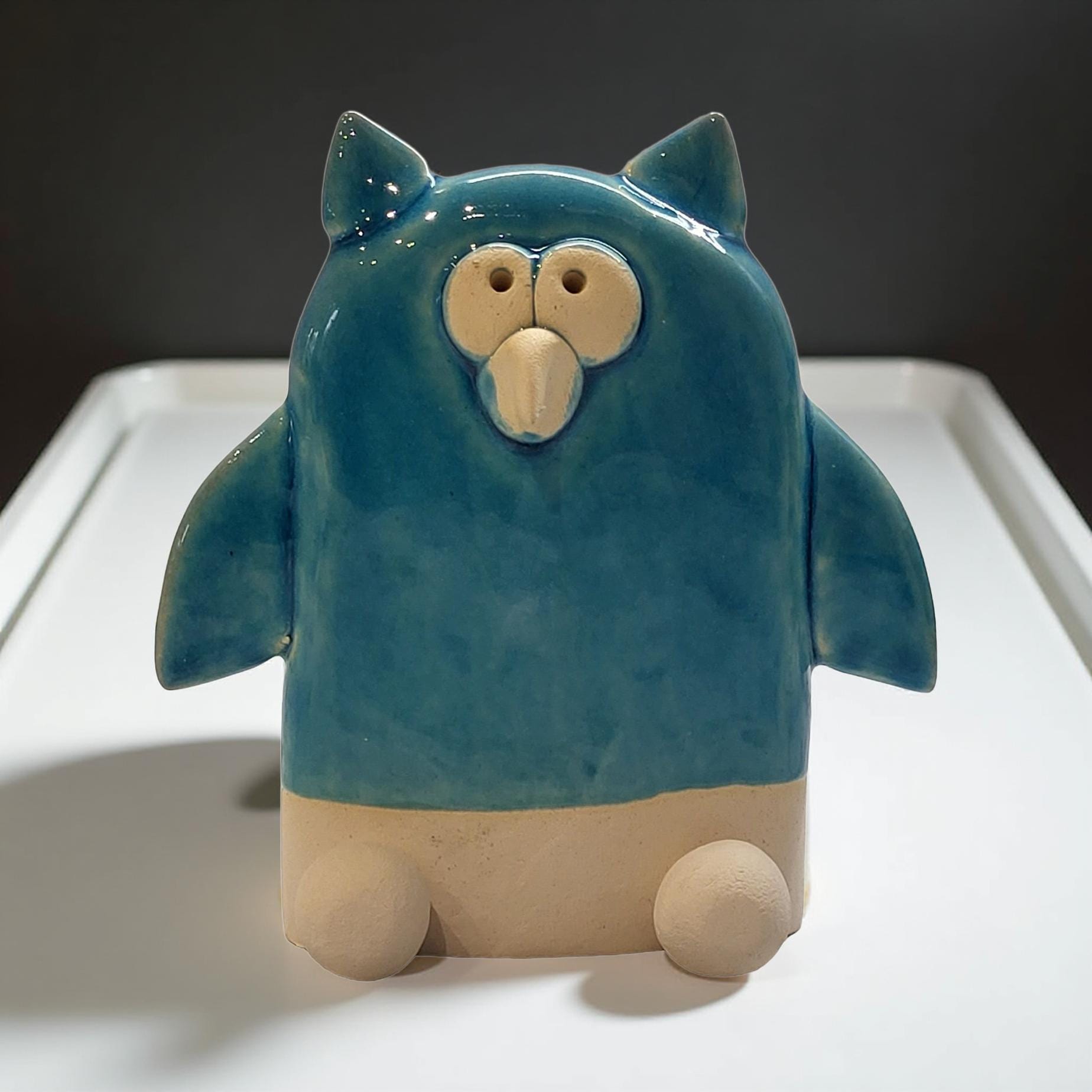 A ceramic owl figurine with a blue body and beige wings, sitting on a white surface.