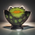 A green frog-shaped glass sculpture with a black and green patterned body, sitting on a black stand against a dark background.