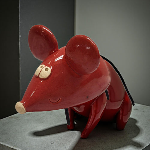A red ceramic mouse figurine with large ears and a small nose is sitting on a gray surface.