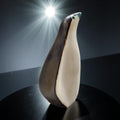 A ceramic penguin figurine is displayed on a black surface, with a bright light shining behind it, creating a dramatic and artistic composition.