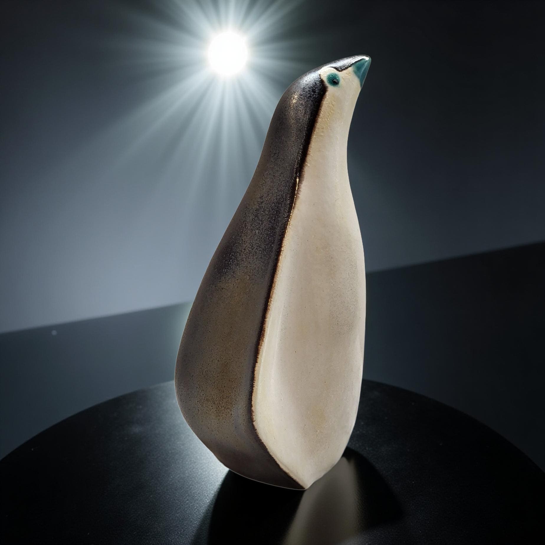 A ceramic penguin figurine is displayed on a black surface, with a bright light shining behind it, creating a dramatic and artistic composition.