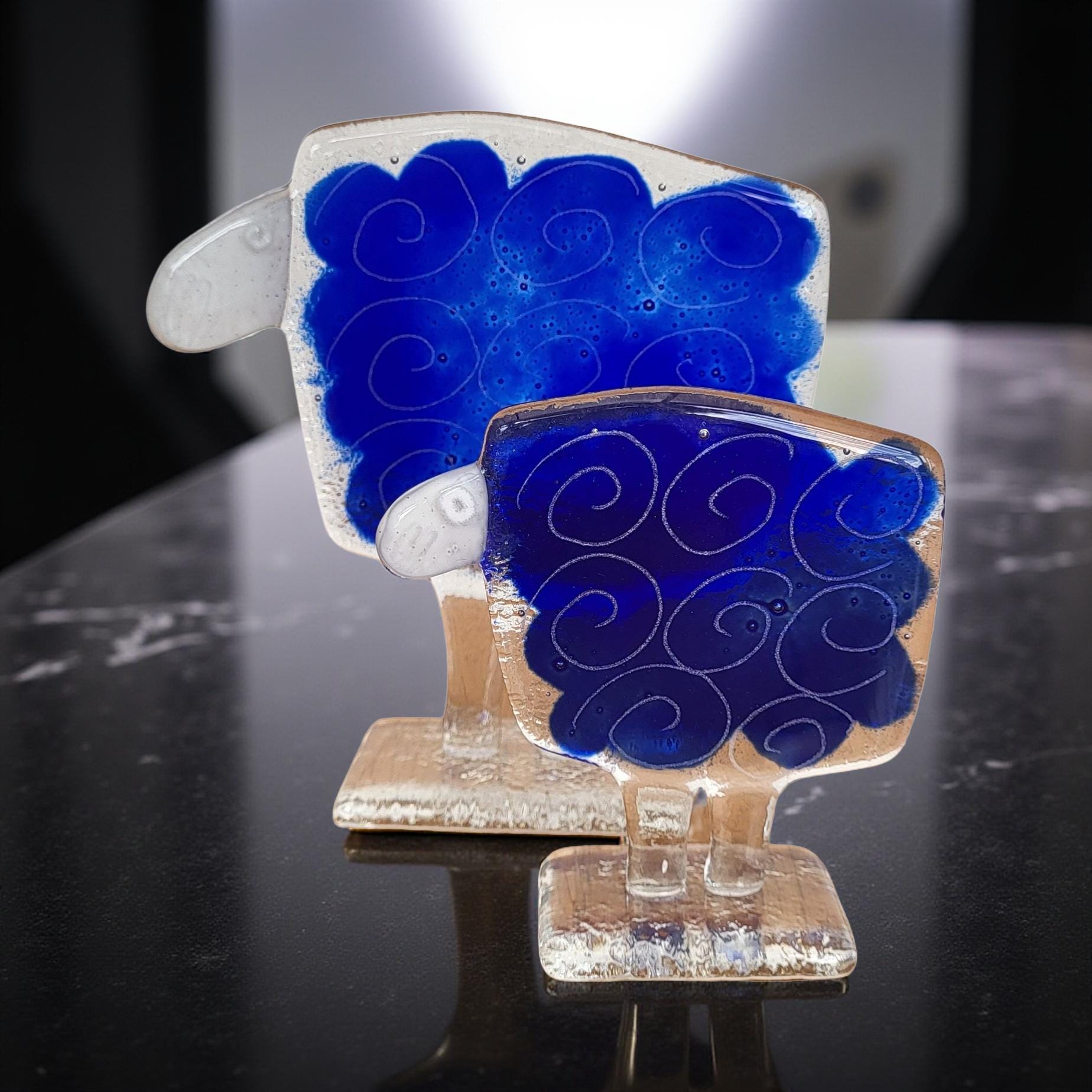 Two glass sculptures of sheep, one larger and one smaller, both with blue swirl patterns on their bodies.