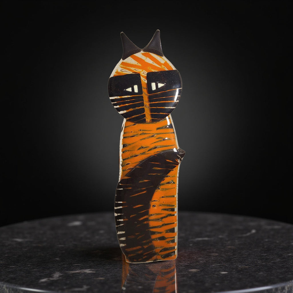 A ceramic cat figurine with a striped pattern and pointed ears is sitting on a dark surface.