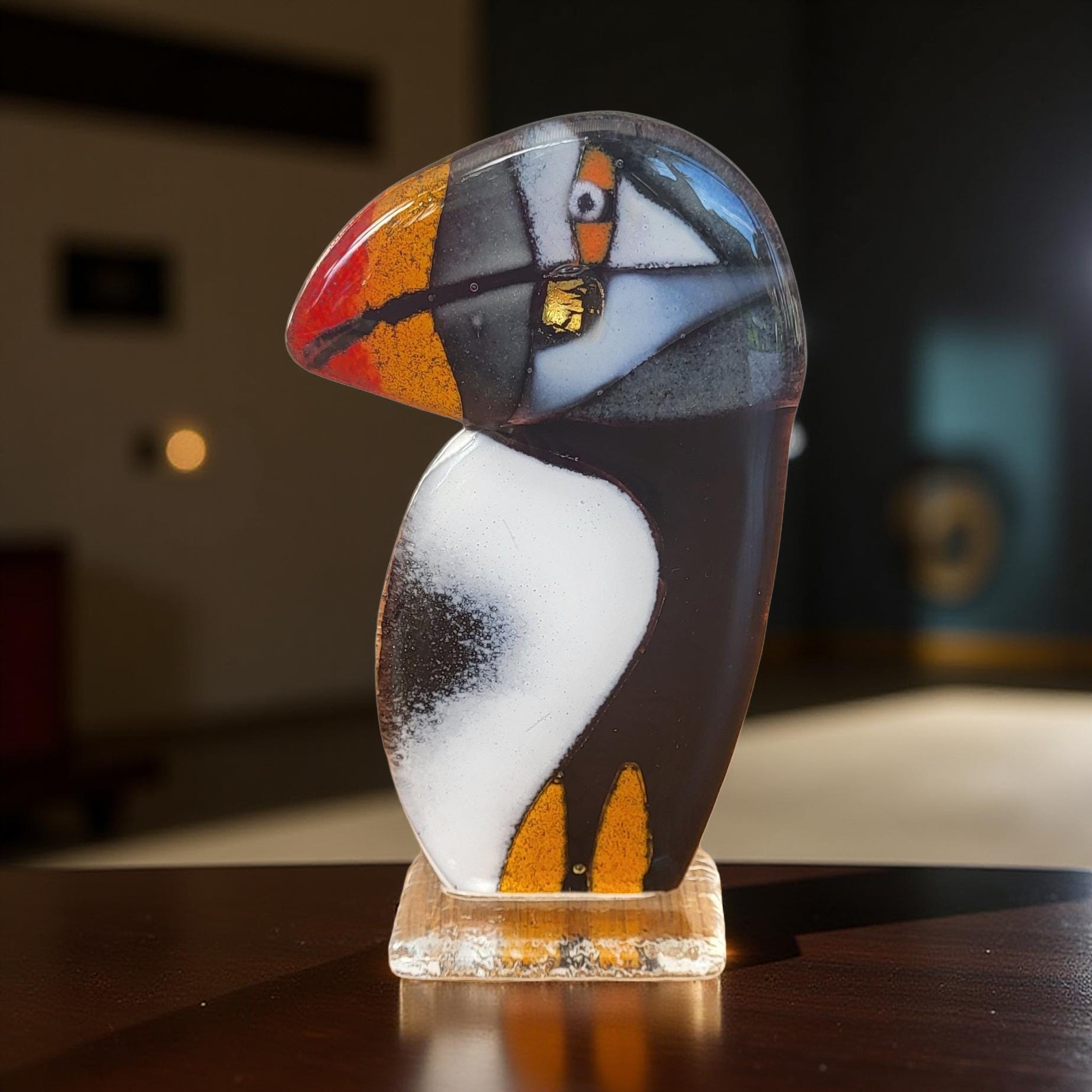 A colorful glass sculpture of a bird, possibly a puffin, is displayed on a wooden surface.