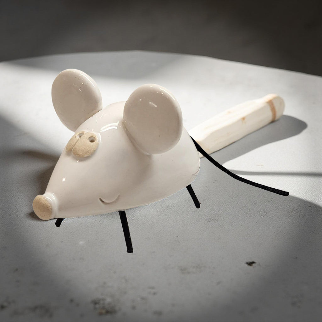 A white ceramic mouse figurine with black legs is sitting on a white surface.