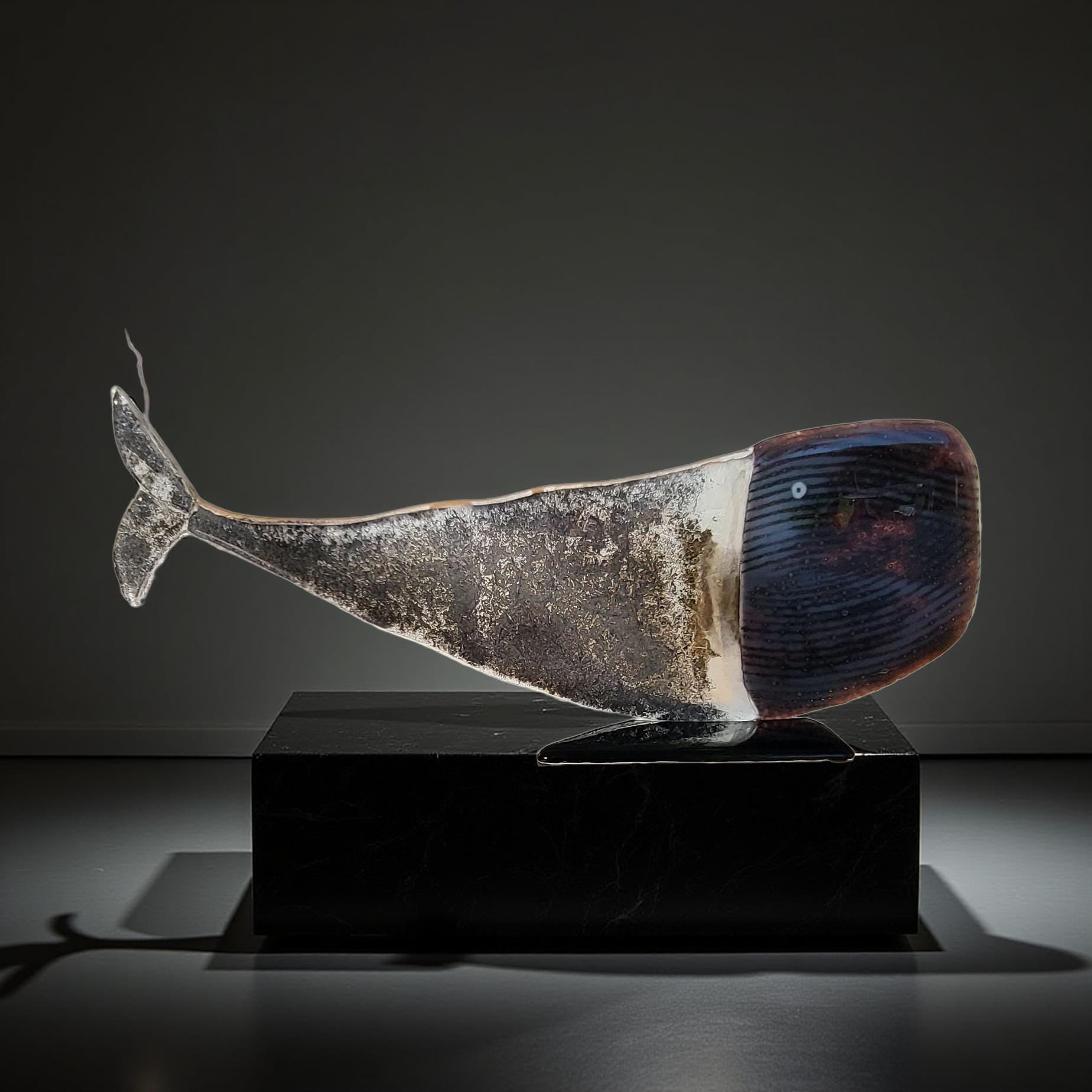 a glass sculpture of a whale, which is displayed on a black pedestal.