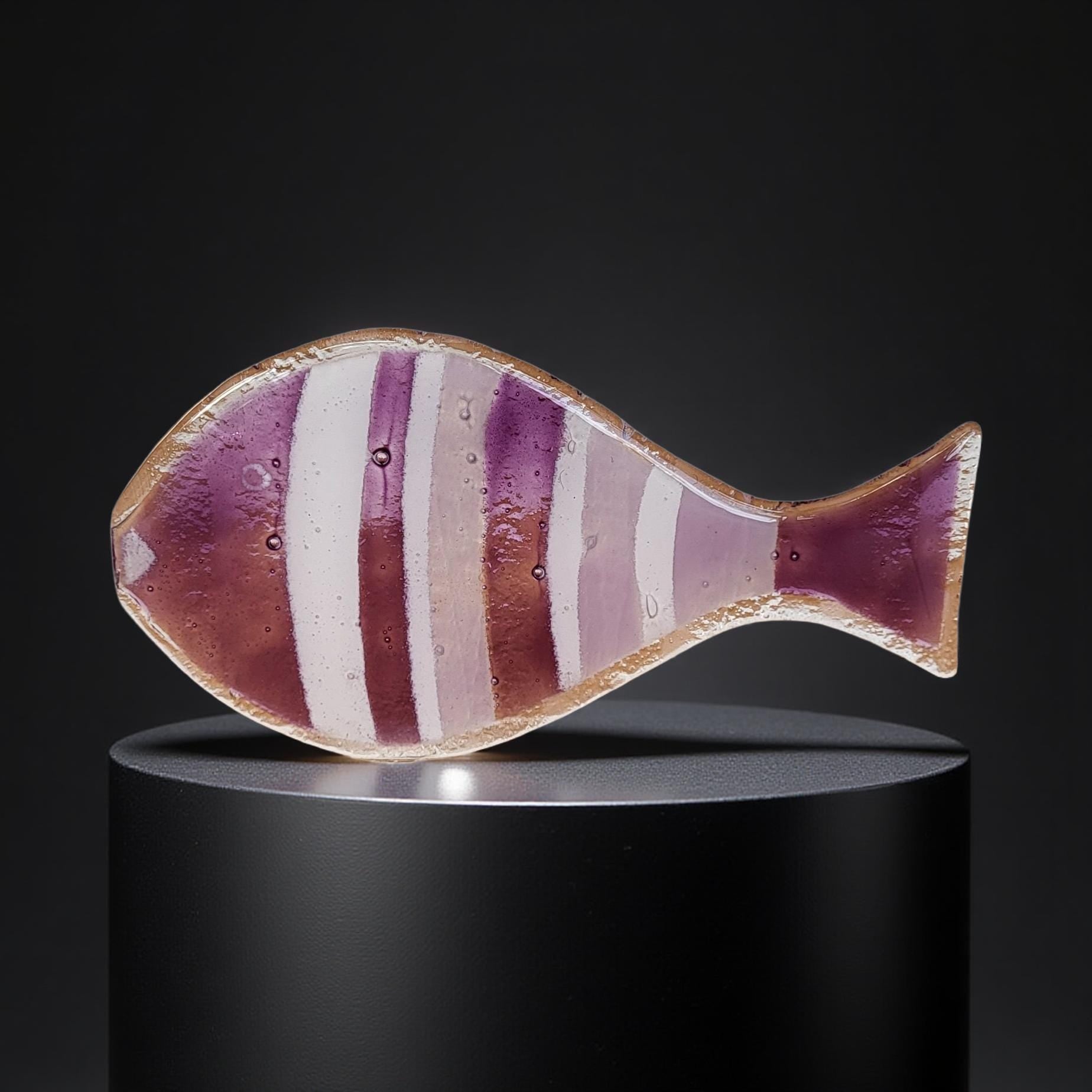A colorful glass fish sculpture is displayed on a black pedestal against a dark background.