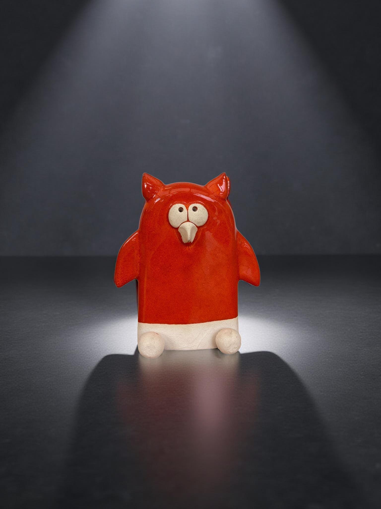 A red ceramic penguin figurine is sitting on a reflective surface against a dark background.