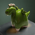 A green ceramic dragon figurine with a white head and tail, sitting on a gray surface against a green background.