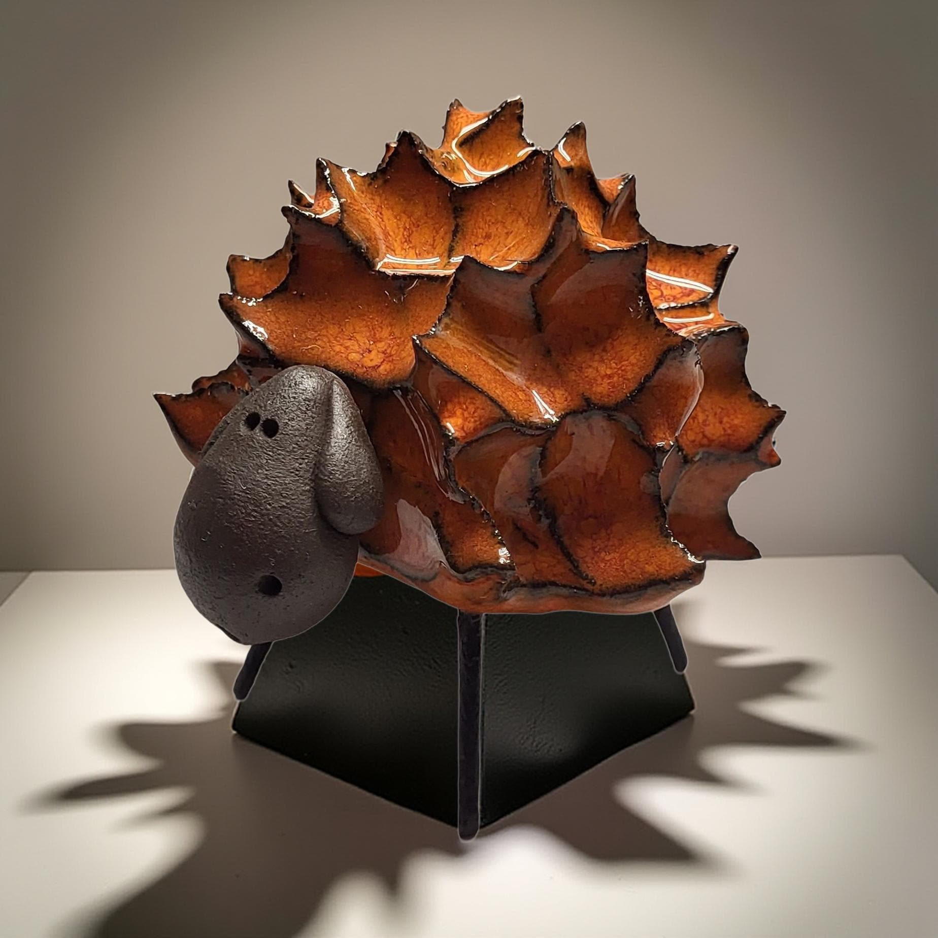 a ceramic sculpture of a sheep with a black nose and mouth, sitting on a black stand.